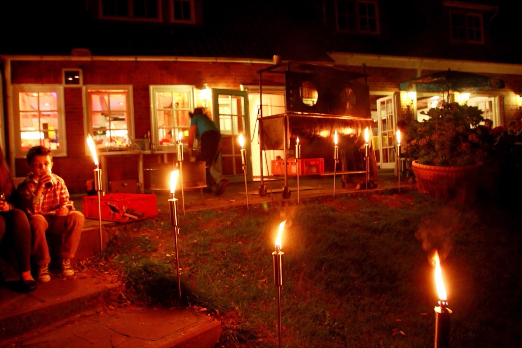 Gäste sitzen am Abend zwischen Fackeln vor dem Haus