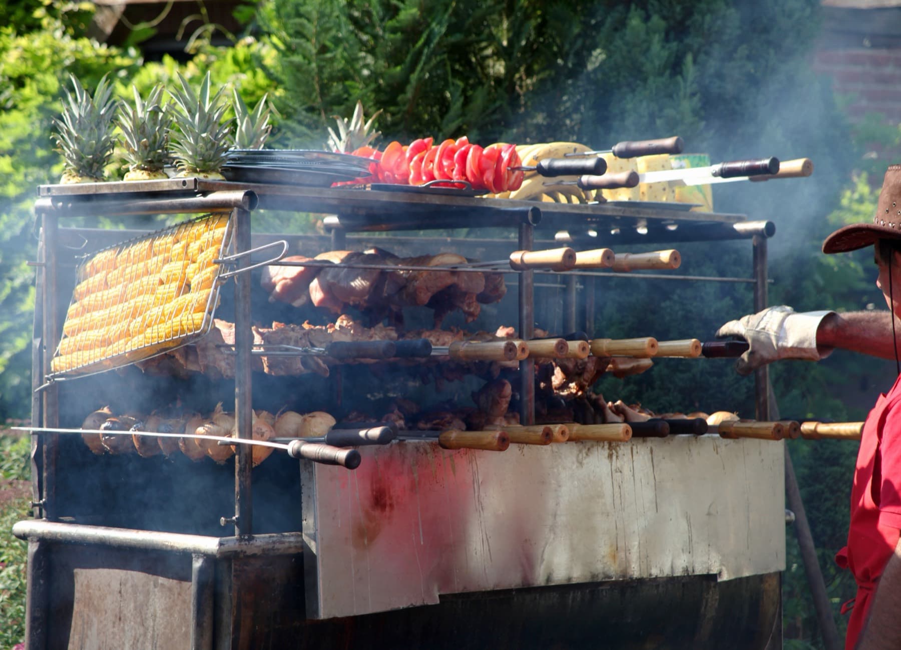 Rauchender Spießgrill mit Maiskolben, Fleisch und Ananas