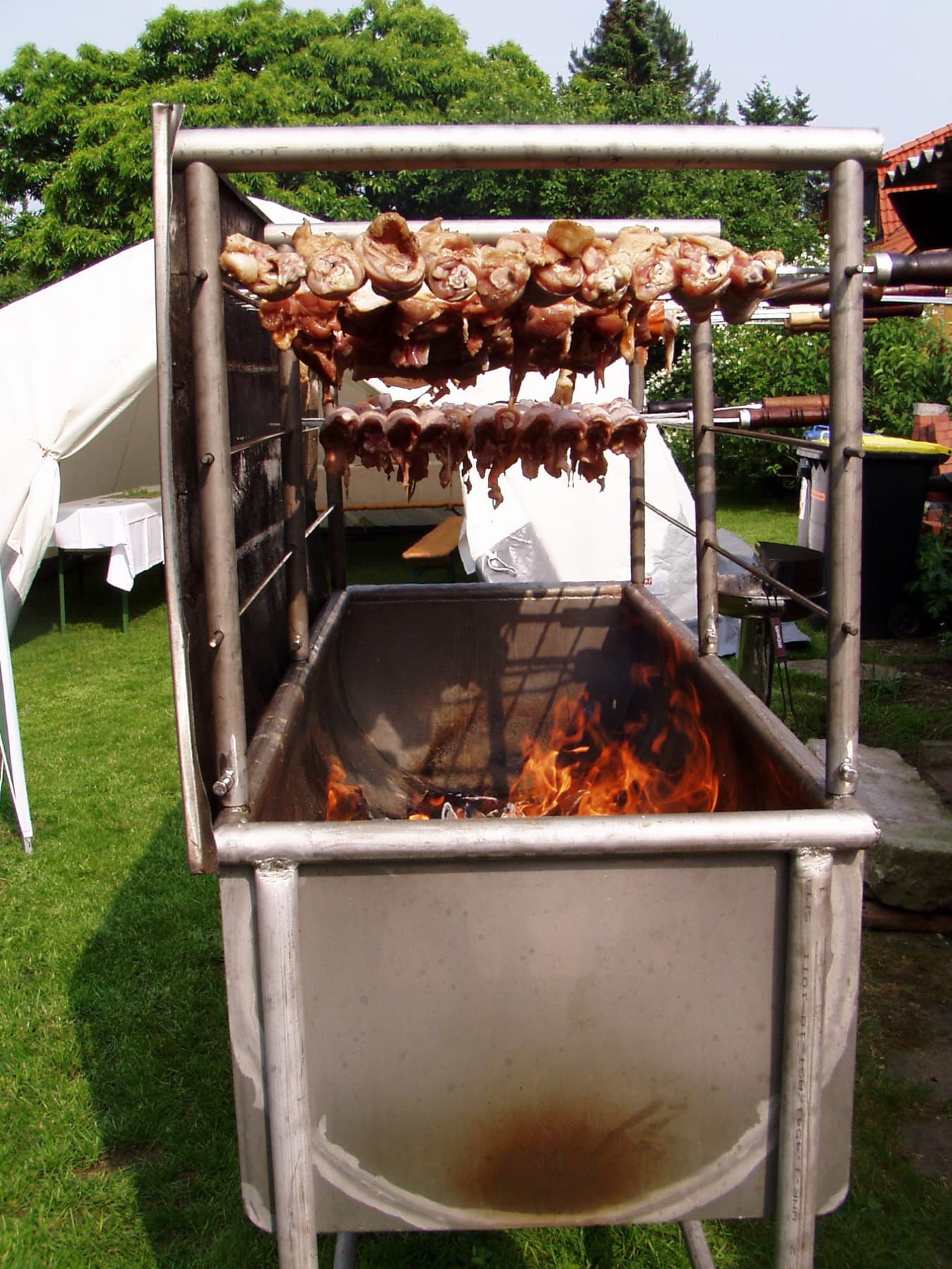 Grill mit Glut und Fleischspießen im Garten neben einem Festzelt